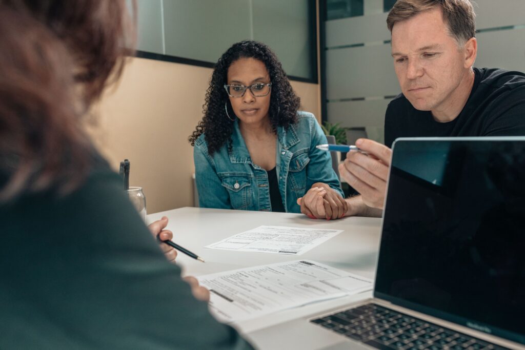 A man and woman hold hands while reviewing paperwork at a desk with a third person.